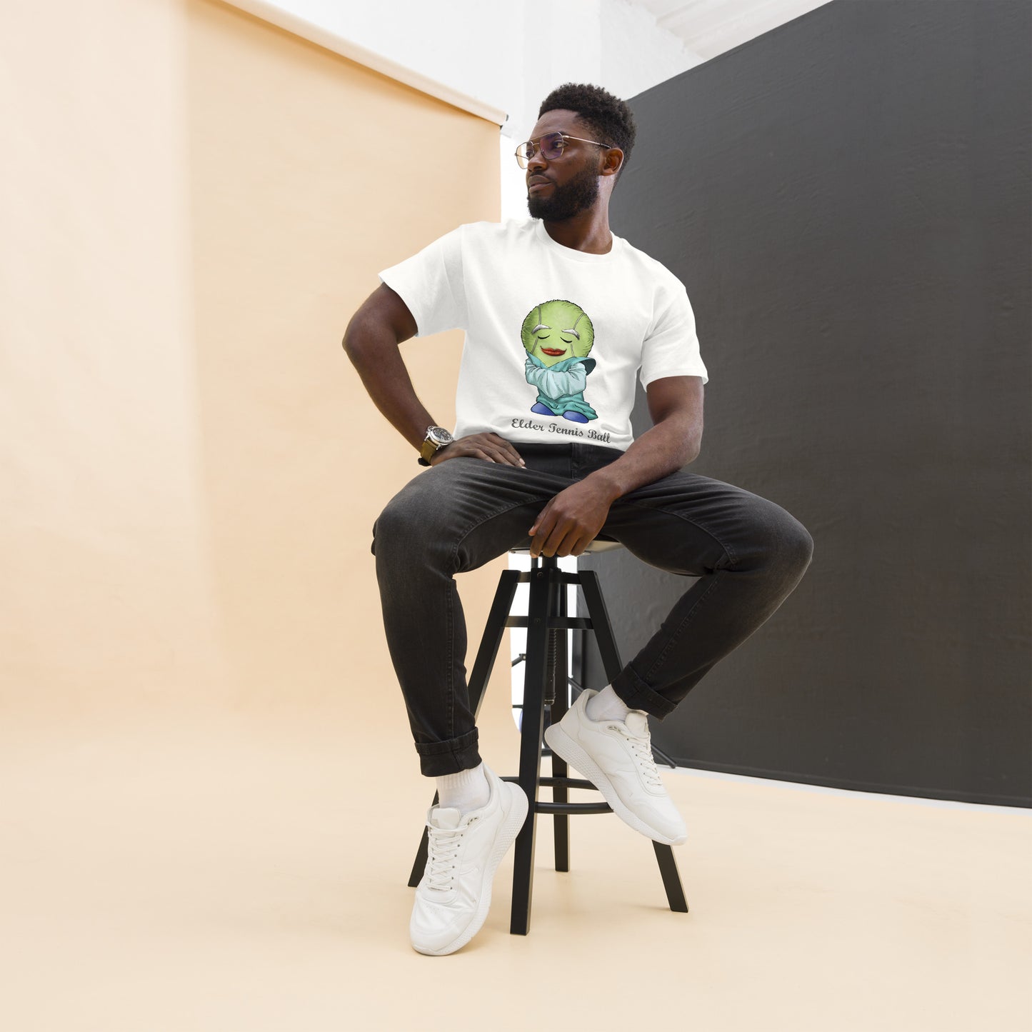Man sitting on a stool wearing a white t-shirt with a Tennis Ball cartoon character print