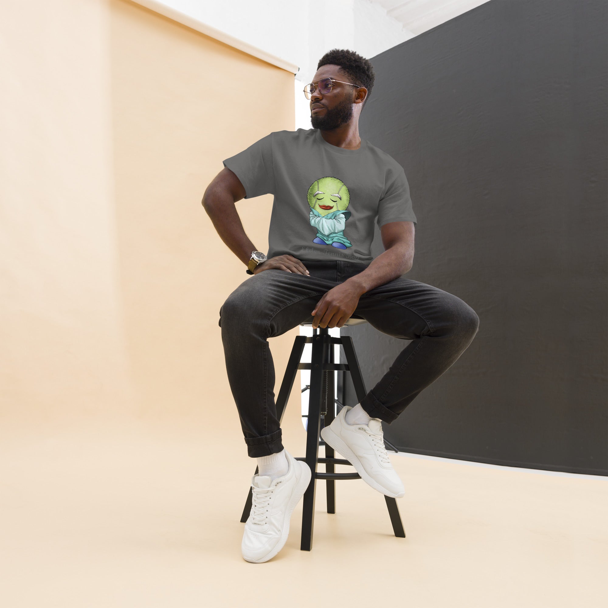 Man sitting on a stool wearing a gray t-shirt with a Tennis Ball cartoon character print 