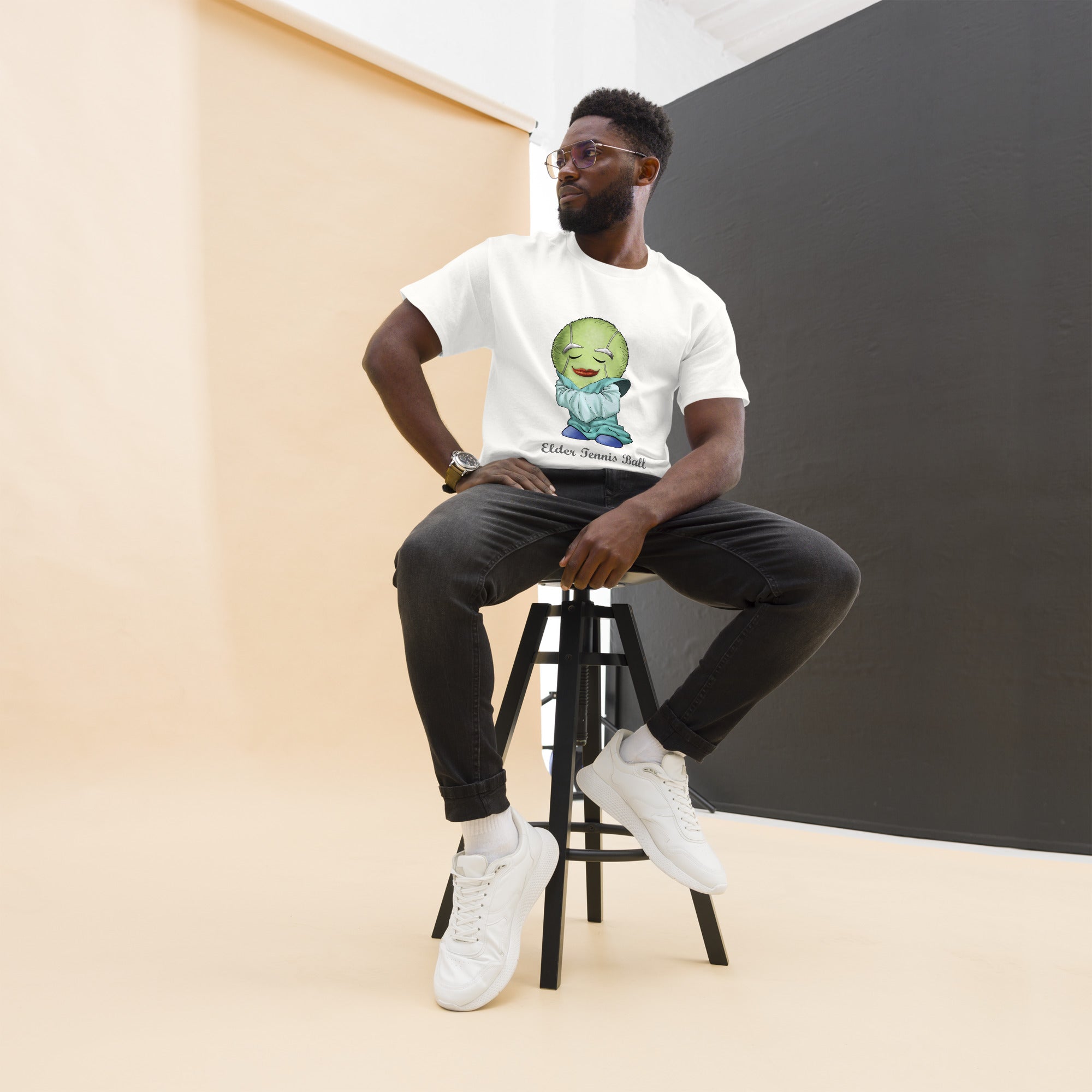 Man sitting on a stool wearing a white  t-shirt with a Tennis Ball cartoon character print 